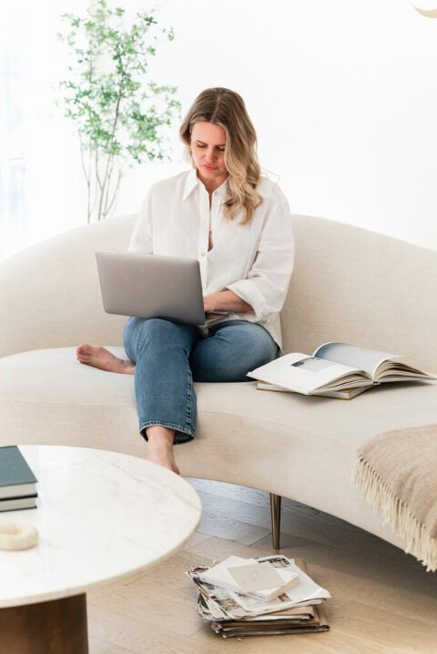Woman Entrepreneur working on website design, on tan couch in white shirt