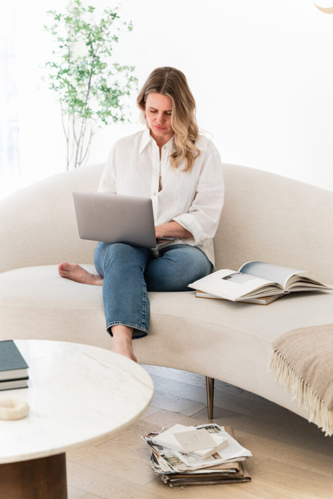 Woman Entrepreneur working on website design, on tan couch in white shirt