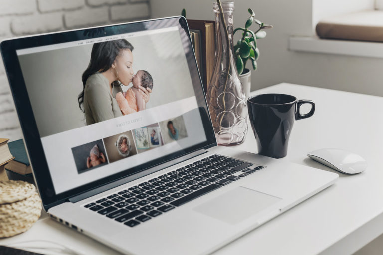 Websites for photographers shown on laptop on desk with coffee mug, showing newborn photography web design on Pro Photo